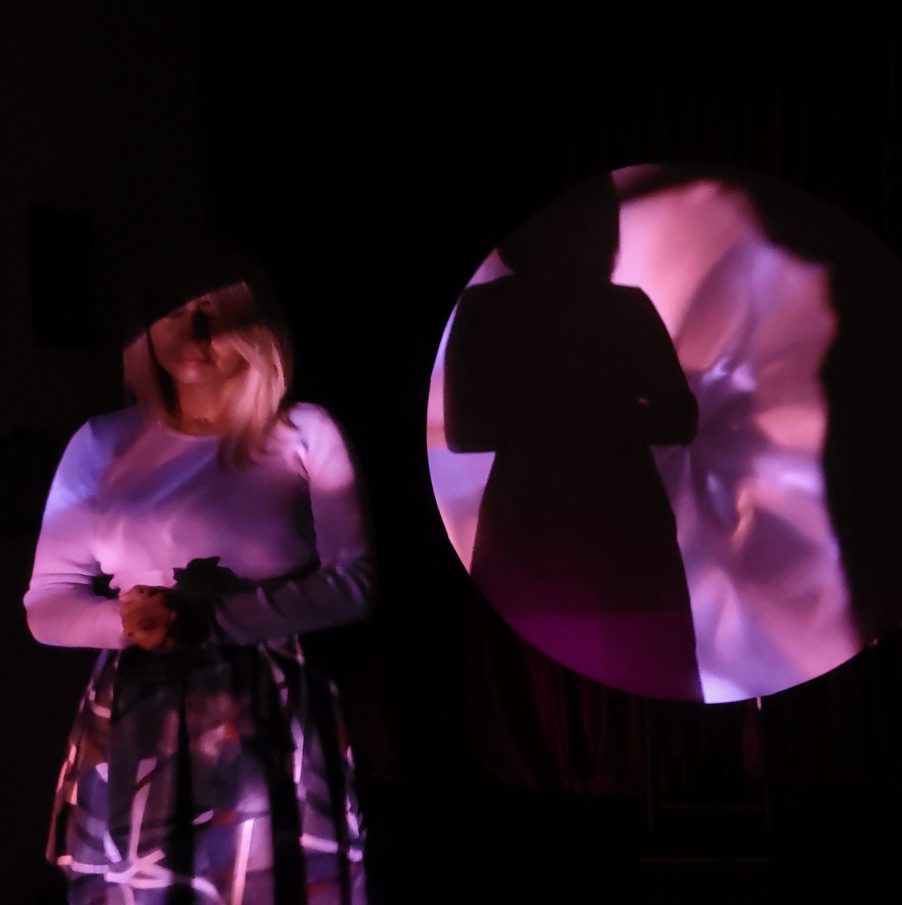 A performer lit by pink and violet projections, beside a round screen showing a silhouette