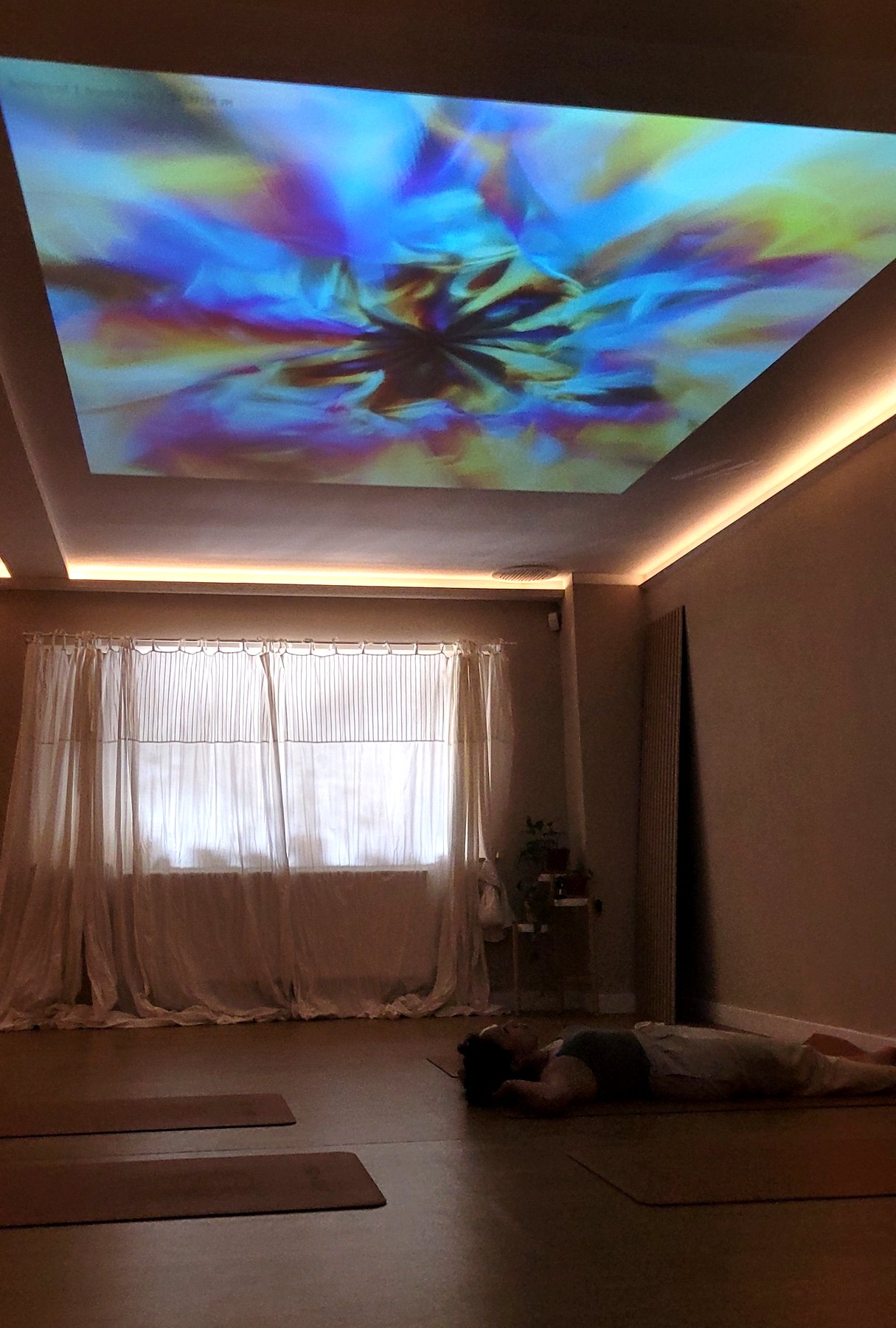 A studio during a session: people lying on mats while colourful visuals are projected across the ceiling