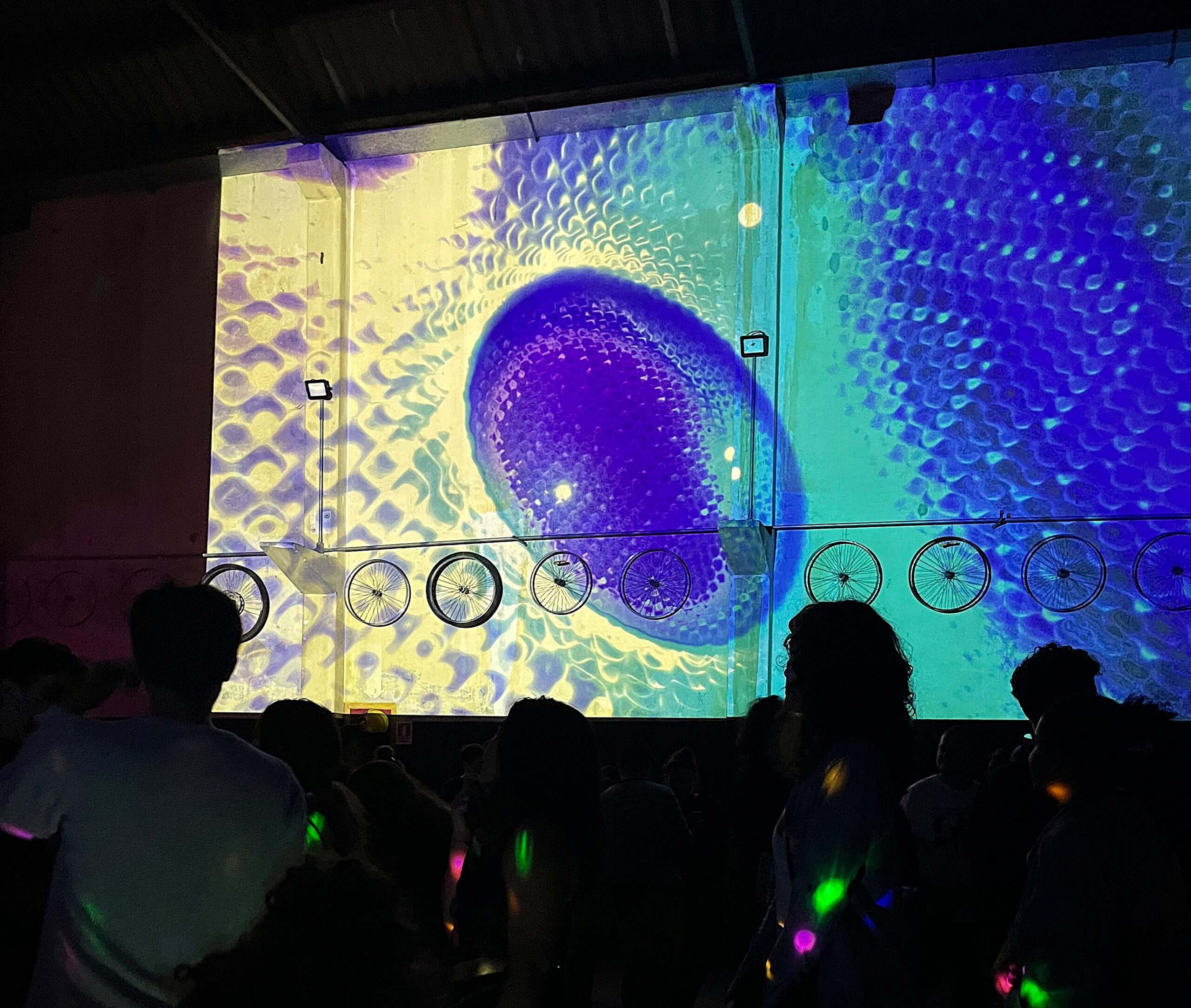 A crowd dancing in front of a wall of blue and yellow projected visuals