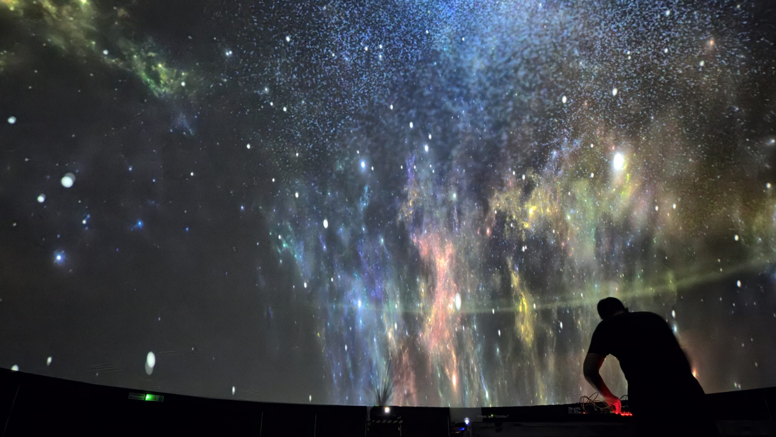 A DJ playing beneath a dome filled with projected stars and nebulae